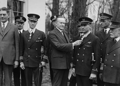 Президент США Калвин Кулидж награждает Почетной медалью Конгресса США прапорщика Флойда Беннетта (справа) и командира Ричарда Э. Бэрда (слева) за первый полет над Северным полюсом, совершенным 9 мая 1926 года. 19 февраля 1927 г.